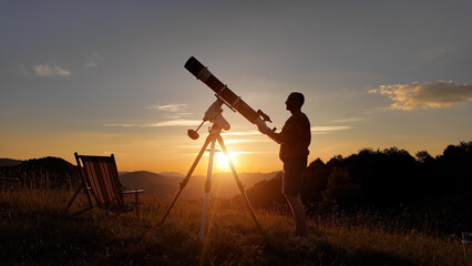 Wall Mural - Amateur astronomer looking at the evening skies, observing planets, stars, Moon and other celestial objects with a telescope just before sun down.