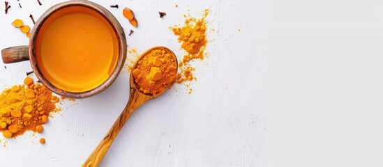 Poster - Top view of a ceramic cup filled with hot Turmeric tea beside a wooden spoon holding turmeric powder displayed on a white background for a health conscious immune boosting concept with a copy space im