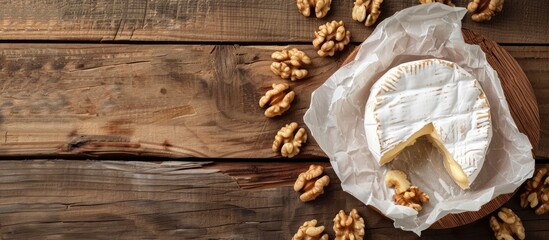Poster - Top down view of Camembert or Brie cheese wrapped in paper with walnuts on a wooden surface for background allowing for copy space image