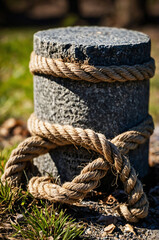 Close-up of thick natural fiber ropes twisted together and tied around a stone post in a grassy outdoor area

