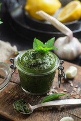 Wall Mural - Green basil pesto sauce in a glass jar on the table