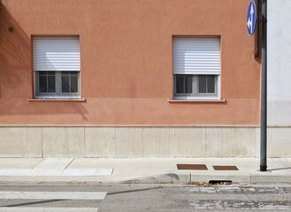 Wall Mural - Brown plaster wall with windows. Arrows traffic sign on the right. Sidewalk and street in front. Background for copy space.