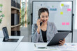 © Wasana - A woman is talking on her cell phone while sitting at a desk with a laptop