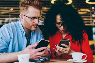 Two multicultural business partners sharing media files on smartphones using bluetooth connection.African american young woman showing caucasian male colleague application on mobile phone device