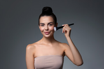 Canvas Print - Beautiful woman applying makeup with brush on grey background