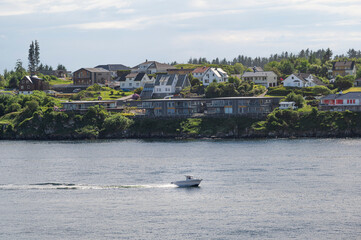 A small speed boat, cruising past residential buildings of the coast of Haugesund, southern Norway, on a bright spring day