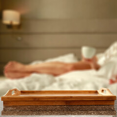 Poster - Close up of wooden table with empty tray with copy space for products. Blurred woman drinking coffee in bed background.  Breakfast in bed concept. 3 d rendering.  