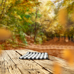 Wall Mural - Old wooden board table with empty copy space for products. Autumn trees in a park background. Image for montage objects display.