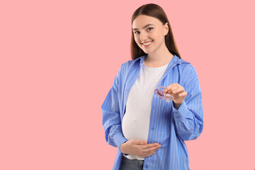 Poster - Expecting twins. Pregnant woman holding two pacifiers on pink background, space for text