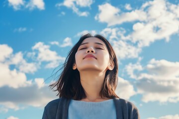 Wall Mural - A woman is looking up at the sky with a smile on her face. The sky is blue with some clouds in the background. The woman is enjoying the moment and taking in the beauty of the sky