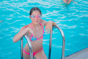 A teenage girl in swimming goggles comes out of the pool. Portrait of a young girl swimmer.