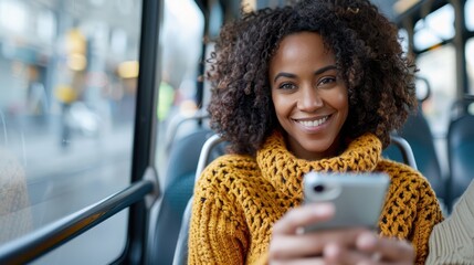 A smiling woman in a yellow sweater is using her phone on a bus. She seems happy and relaxed, interacting with her device during the commute on public transportation.