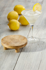 Wall Mural - Yellow lemons and drink in cocktail glass on wooden table. Close up andround wooden stand with copy space for food and drinks and products. 