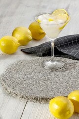 Wall Mural - Drink in cocktail glass on flat stone and scattered yellow lemons on white wooden table. Close up and copy space for food and drinks and products. 