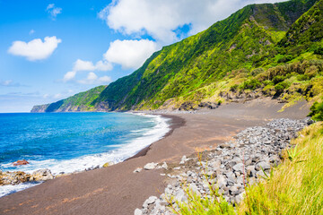 Wall Mural - Black sand volcanic beach of Faja and green tropical landscape with high cliffs on ocean coast, Faial island, Azores, Portugal