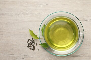 Poster - Refreshing green tea in cup and leaves on wooden table, flat lay. Space for text