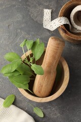 Wall Mural - Green sage leaves in mortar with pestle on grey textured table, flat lay