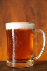 Wall Mural - Mug with fresh beer on wooden table against color background, closeup