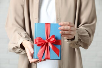 Wall Mural - Woman holding book tied with red ribbon indoors, closeup