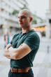 © qunica.com - Confident young business entrepreneur in outdoor meeting, wearing green polo shirt, standing with arms crossed in urban setting.