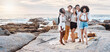 © peopleimages.com - Friends, group and happy for picnic on beach with laughing, bonding and hugging on holiday and vacation banner. People, diversity and portrait with drinking alcohol on rocks for relax or summer break