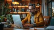 © Vladan - Middle-aged man in a smart blazer, focused on his laptop in a warmly lit home office, surrounded by plants and books. Ideal for remote work themes.