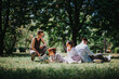 © qunica.com - Group of friends enjoying a relaxed summer day at the park, surrounded by trees and sunlight