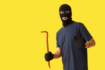 Wall Mural - Male thief with crowbar on yellow background