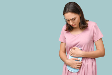 Sticker - Young woman with hot water bottle suffering from menstrual cramps on blue background