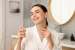 © New Africa - Smiling woman spraying aromatic perfume in bathroom