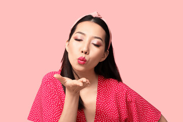 Poster - Beautiful Asian woman with stylish makeup blowing kiss on pink background