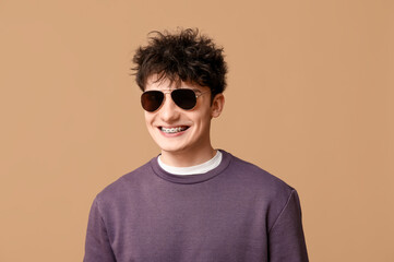 Wall Mural - Handsome young man in stylish clothes and sunglasses on brown background