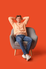 Canvas Print - Handsome young man relaxing and sitting in armchair on orange background