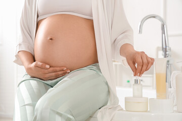 Canvas Print - Young pregnant woman with skincare products sitting on bathtub at home, closeup