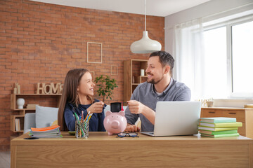 Canvas Print - Father and his daughter holding mortar board on piggy bank at home. Tuition fees concept