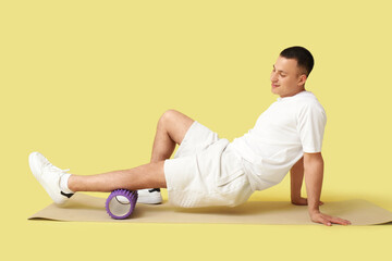 Poster - Sporty young man training with foam roller on mat against yellow background