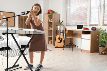 Wall Mural - Cute little girl with microphone and modern synthesizer singing at home