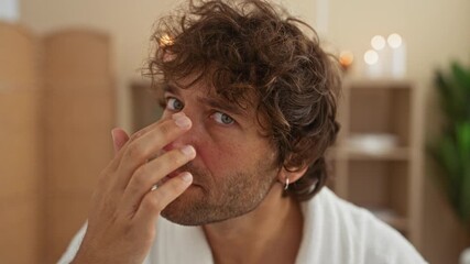 Wall Mural - Young man in a spa room with candles and plants touching his nose and looking relaxed