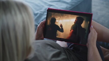 Poster - adult woman watches action movie using tablet computer while lying on sofa. digital tablet screen wi