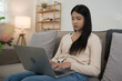 © snowing12 - Young asian women putting laptop on legs and typing business report about marketing data of new startup while sitting on the couch to spending time and relaxation with enjoying lifestyle at home