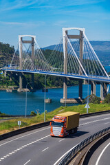 Canvas Print - Truck with container driving on the highway with the Rande Bridge in the background, Vigo.