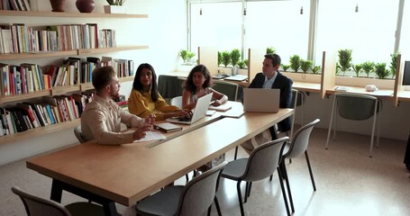 Wall Mural - Group of diverse adult students meeting in library, working on training group project. Multiethnic business team talking in co-working space, discussing teamwork at large table. High angle view