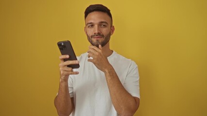 Poster - Smart young hispanic man pointing finger with happy face, smartphone in hand, number one idea over isolated yellow background