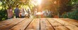 © Simon - Empty wooden table and blurred view of a group of people having BBQ barbecue outdoors. Wood desk in front of a natural garden background. Summer lifestyle concept.