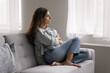 © fizkes - Serious pensive young woman thinking on problem, hugs cushion seated on couch at home, deep on sad thoughts, staring out window, looks depressed, frustrated, misses her beloved, feels lonely. Solitude