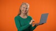 © Robert Peak - Portrait of happy excited jubilant fun mature blonde woman 40s 50s years old using work on laptop pc computer isolated on orange background studio