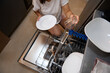 © Taras Grebinets - Woman unloading dishwasher with white plates and glass cups in modern kitchen setting