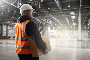 Poster - Man warehouse contractor. Guy with cardboard box works in storage. Contractor walks through warehouse hangar. Empty storehouse of manufacturing company. Man loader carries box to warehouse