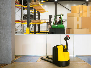 Wall Mural - Electric pallet jack in warehouse. Equipment for unloading. Pallet jack in industrial building. Warehouse with cardboard boxes. Pallet jack for loading pallets into machine. Storage area