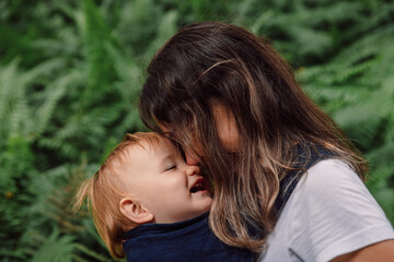 Portrait of Mother with her cute baby in park between fern leaves